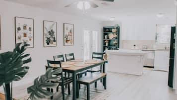 Cozinha moderna com armários brancos, uma ilha central e um espaço de refeições com mesa e cadeiras de madeira.
