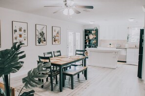 Cozinha moderna com armários brancos, uma ilha central e um espaço de refeições com mesa e cadeiras de madeira.