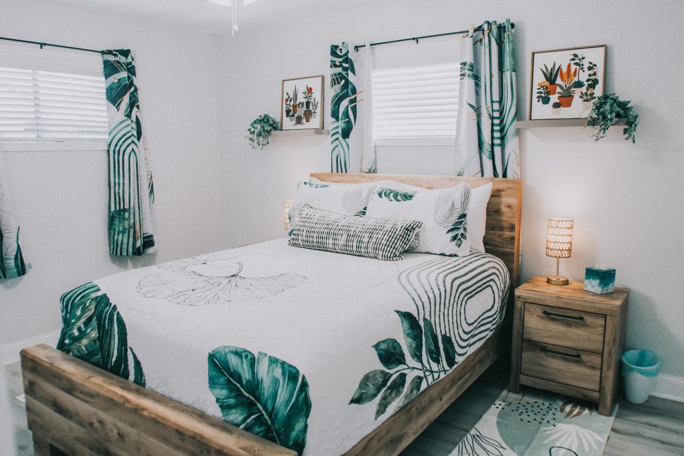 A bedroom with a bed, a nightstand, a lamp, and wall decorations including framed pictures and a plant.