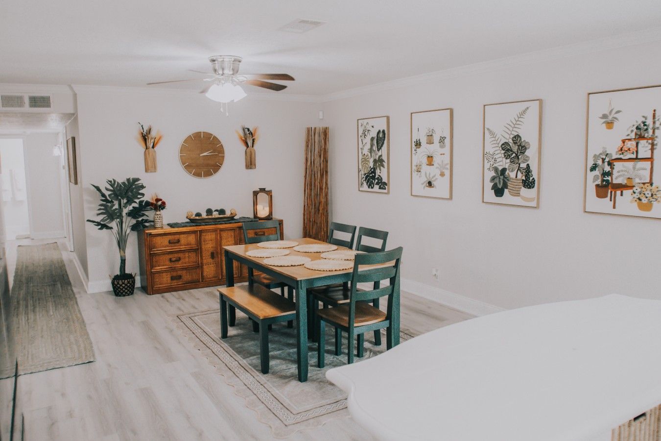 A dining area with a wooden table and chairs, a ceiling fan, and framed botanical prints on the wall.