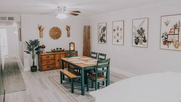 A dining area with a wooden table and chairs, a ceiling fan, and framed botanical prints on the wall.