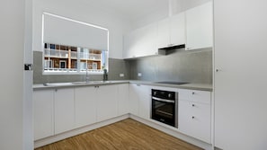 Moderni keittiö, jossa on valkoiset kaapit, sisäänrakennettu uuni ja ikkuna, josta avautuu näkymä parvekkeelle.