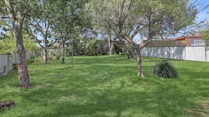 A backyard with a lawn, trees, a swing set, and a white fence. - The White Honey Cottage - Newly Renovated 4BDR on White Street (West Tamworth)