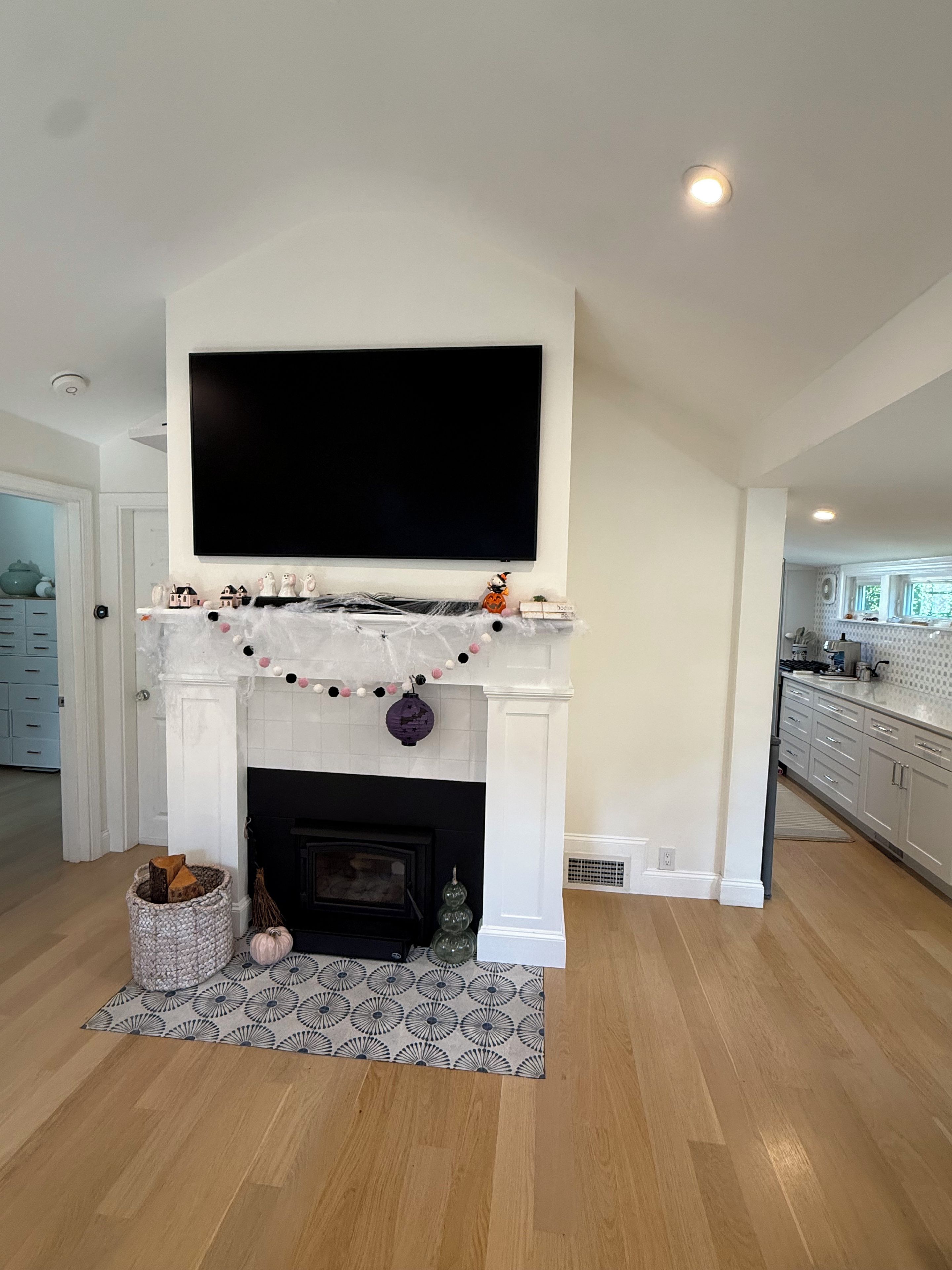 A living room with a fireplace, a mounted television, and a kitchen in the background.
