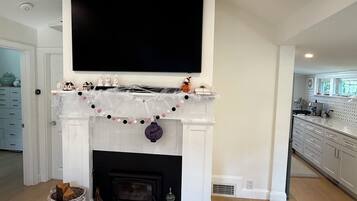 A living room with a fireplace, a mounted television, and a kitchen in the background.