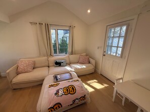 Ett mysigt vardagsrum med en beige soffa, ett litet bord och ett fönster med gardiner.