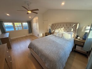 Une chambre à coucher avec un grand lit, un ventilateur de plafond, une table de chevet avec une lampe et une fenêtre avec des rideaux.