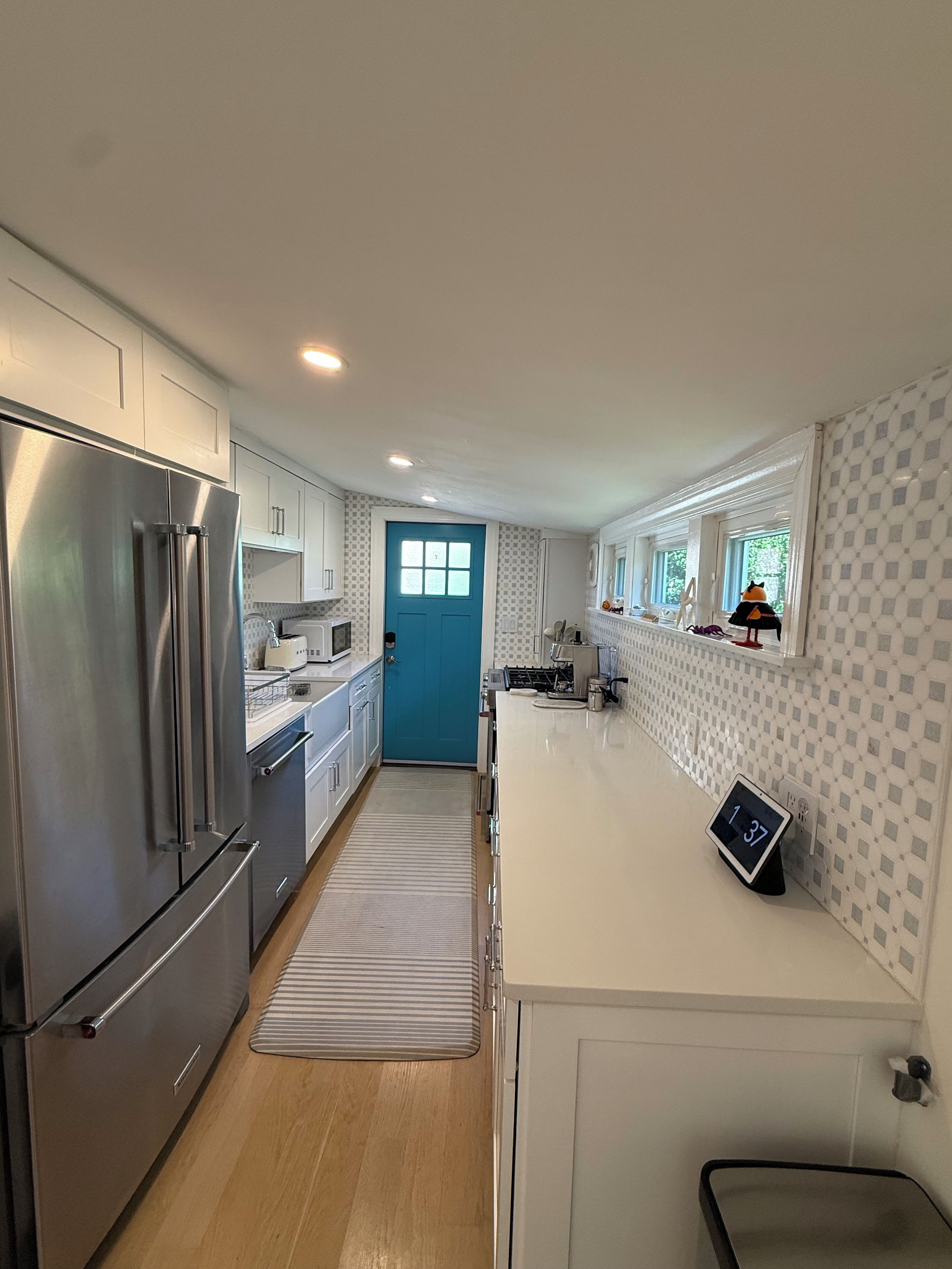 A modern kitchen with stainless steel appliances, a blue door, and a digital clock.