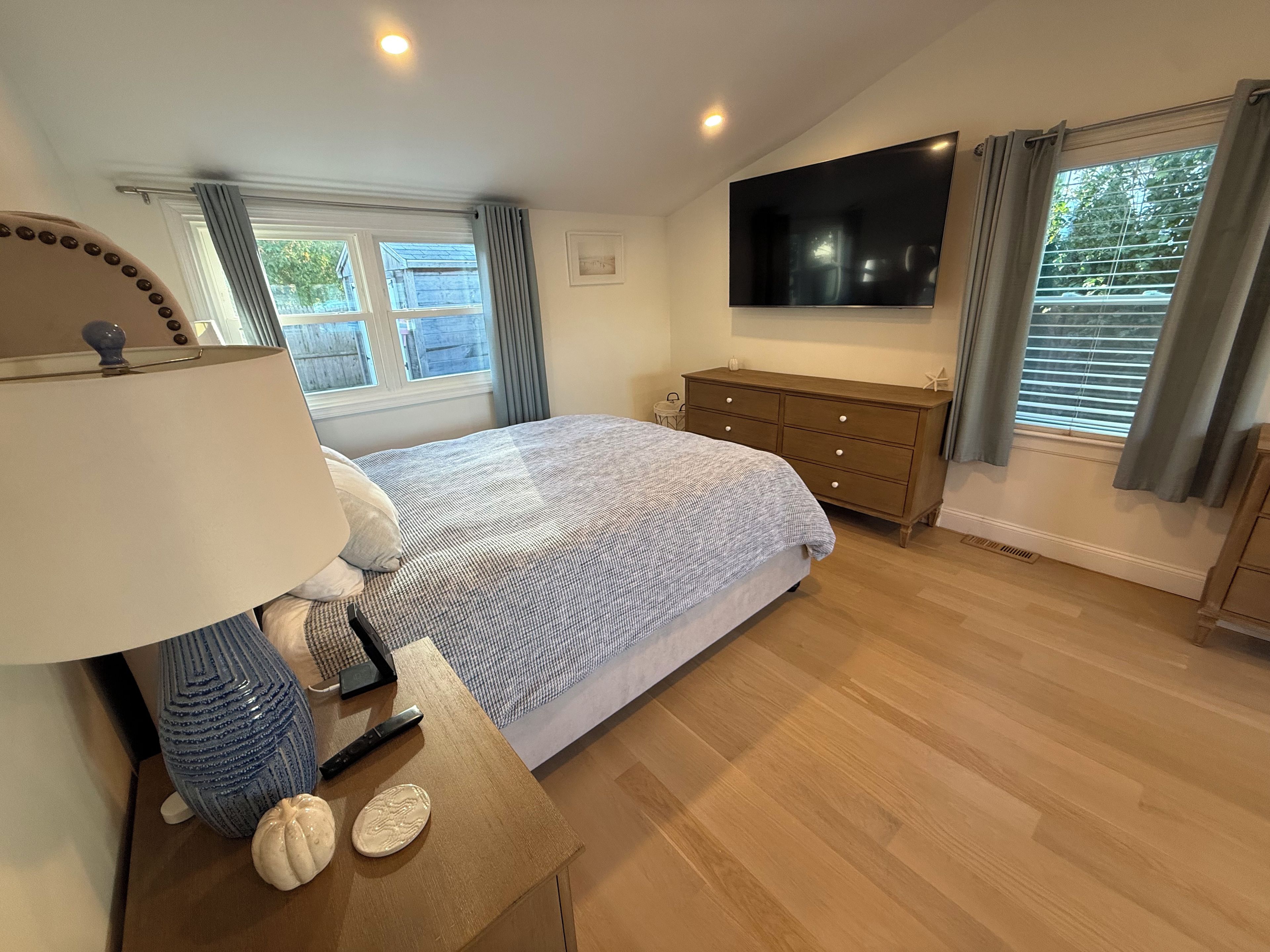 A bedroom with a bed, a TV mounted on the wall, a dresser, and a window with curtains.