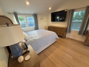 A bedroom with a bed, a TV mounted on the wall, a dresser, and a window with curtains. - Coastal Marblehead Retreat, Minutes to Salem, Beautifully Renovated (Marblehead)