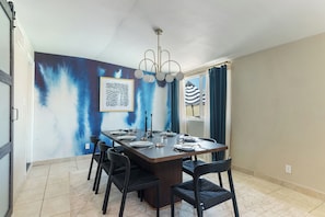 A dining area with a rectangular table set for four, surrounded by chairs, with a ceiling light fixture above. - Private pool paradise w/ping pong, foosball & outdoor fire pit! (Tempe)