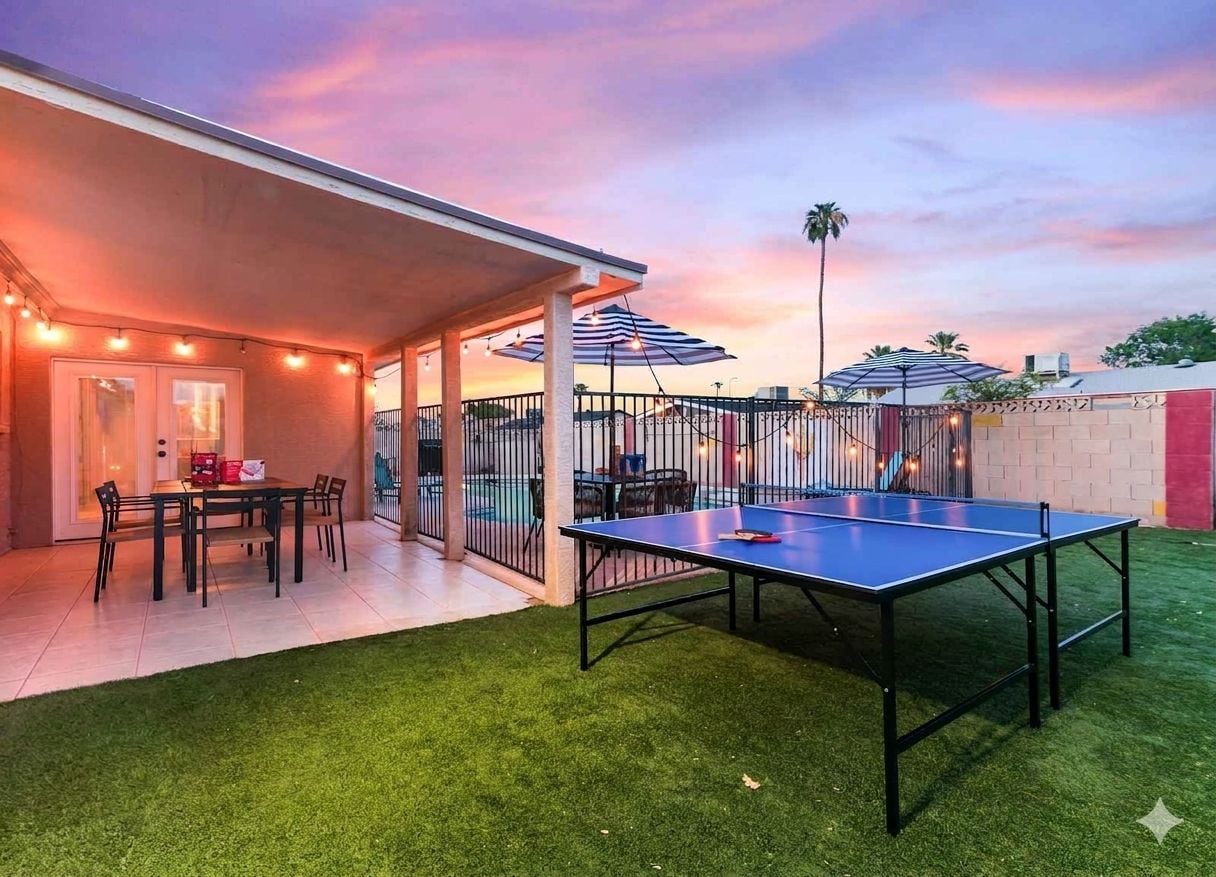 Un patio exterior con mesa de ping pong, zona de estar techada y luces colgantes.