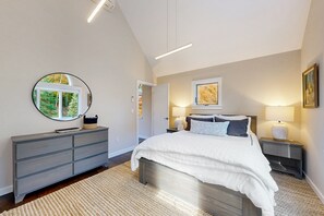 A bedroom with a bed, bedside tables, a dresser, a round mirror, and artwork on the walls. - Luxury Ludlow Retreat | Hot Tub, private gym, sauna Near Okemo (Ludlow)