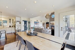 A modern kitchen with a central island, a dining area with chairs, a living room with a sofa, and a fireplace. - Luxury Ludlow Retreat | Hot Tub, private gym, sauna Near Okemo (Ludlow)