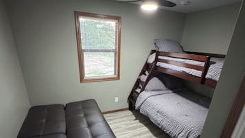 A room with a bunk bed, a sofa, a ceiling fan, and a window with blinds.