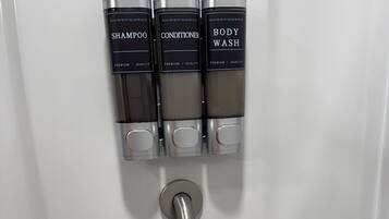 Eine wandmontierte Spenderstation mit drei Fächern, beschriftet mit 'SHAMPOO', 'CONDITIONER' und 'BODY WASH'.