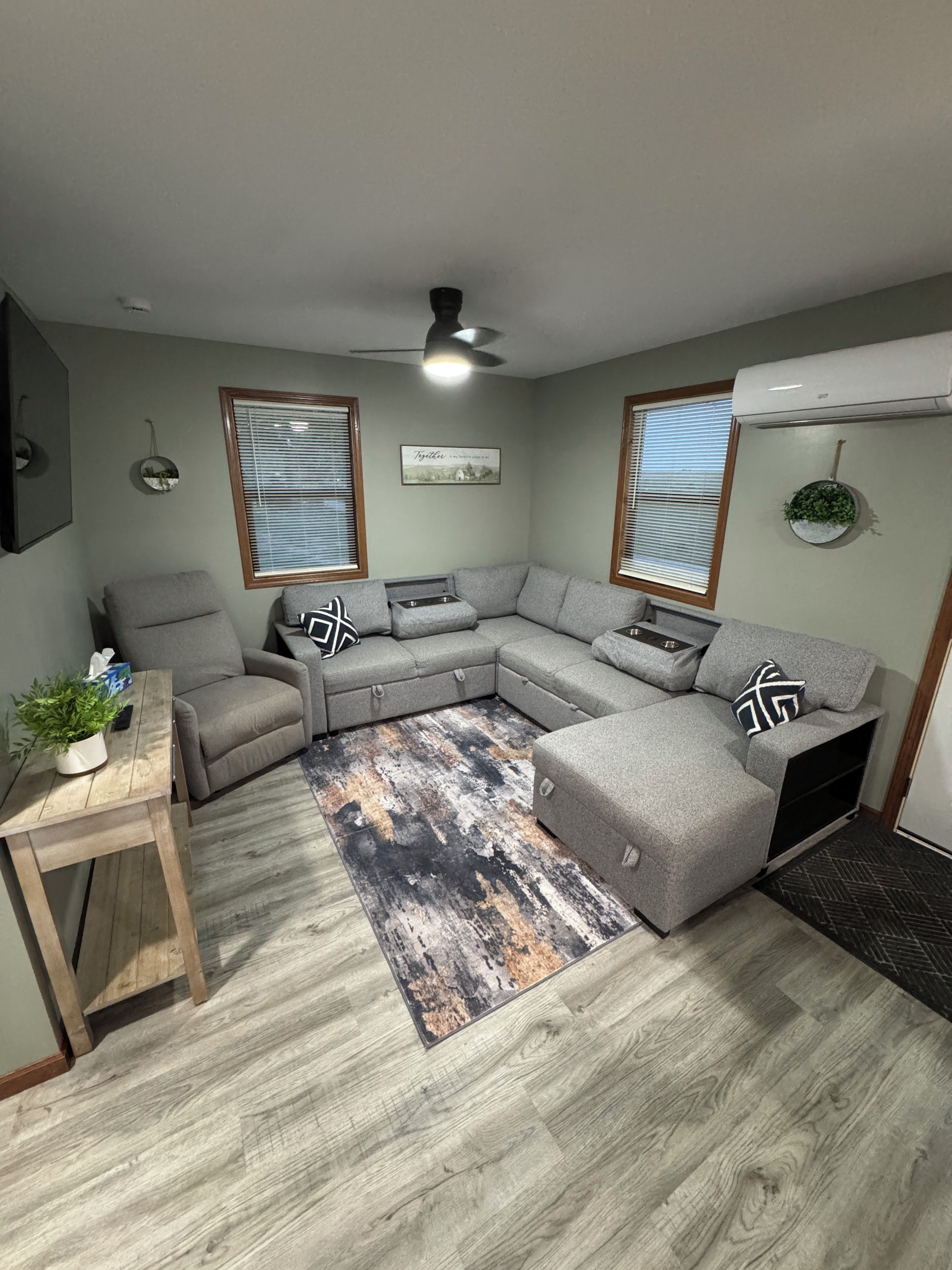Una sala de estar con un sofá seccional gris, una mesa de centro de madera y un tapete estampado.