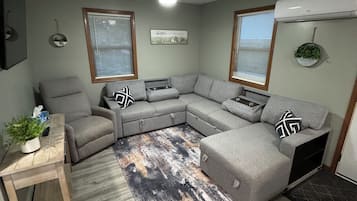 Una sala de estar con un sofá seccional gris, una mesa de centro de madera y un tapete estampado.