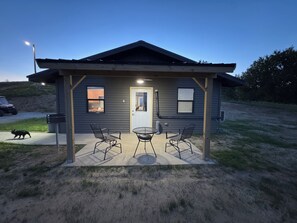 Een klein houten huisje met een veranda, twee stoelen en een tafel.