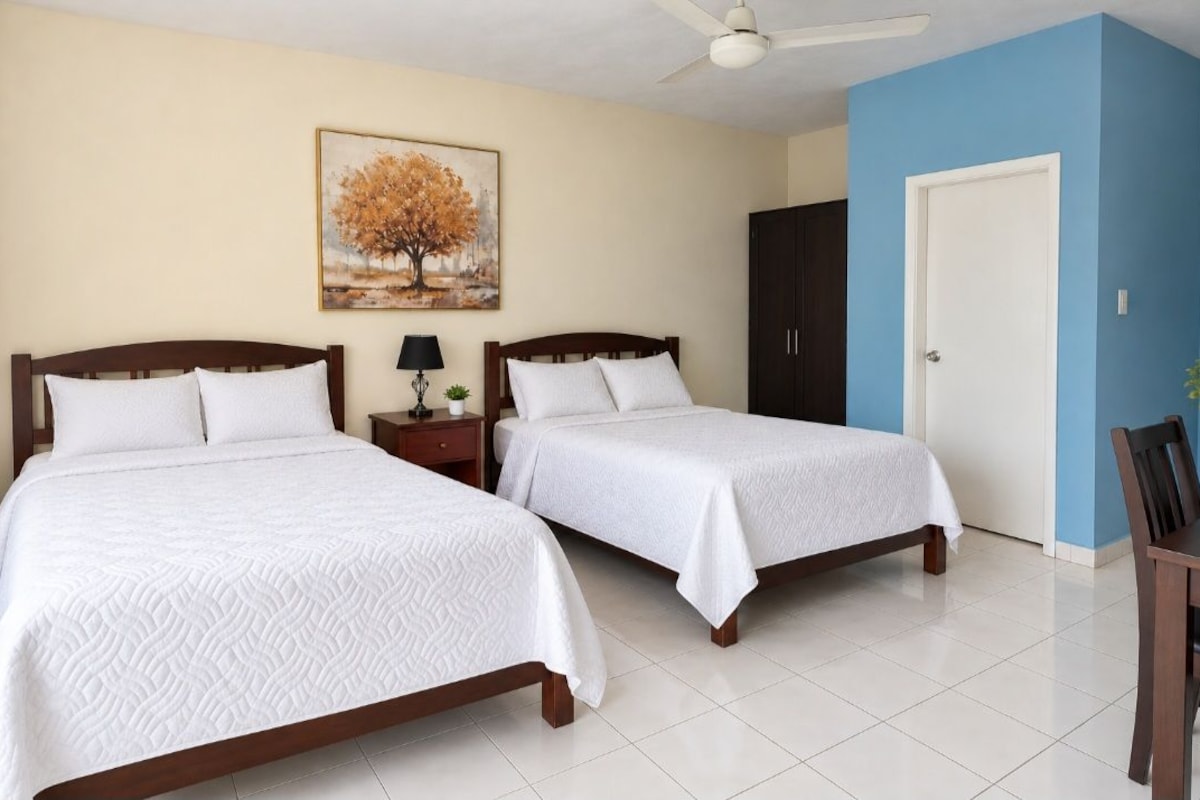 A hotel room with two beds, a nightstand, a lamp, a painting, a wardrobe, and a door.