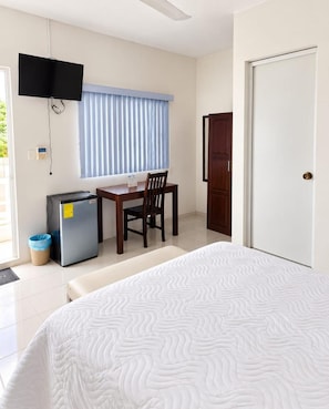 A bedroom with a bed, a desk with a chair, a television mounted on the wall, and a door.