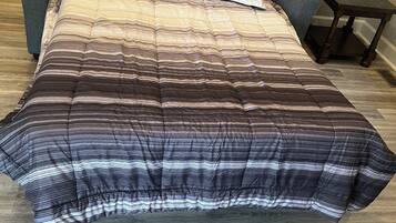 A bed with a striped comforter, a gray sofa, and a small wooden nightstand.