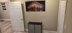 A hallway with a closed door, a wall-mounted picture of a tree, and a filing cabinet.