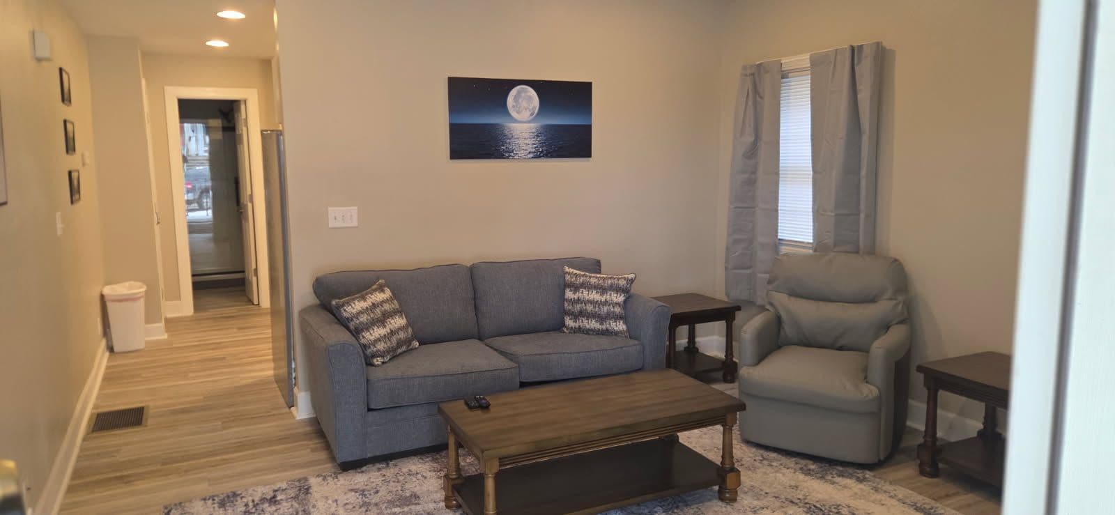 A living room with a sofa, armchair, coffee table, and a painting of the moon on the wall.