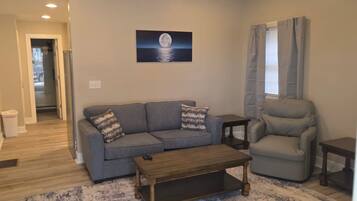 A living room with a sofa, armchair, coffee table, and a painting of the moon on the wall.