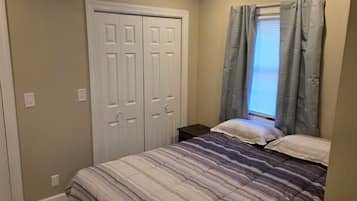 A bedroom with a bed, two doors, and a window with curtains.