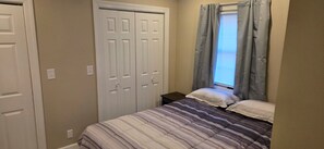 A bedroom with a bed, two doors, and a window with curtains.