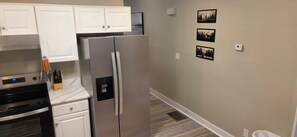 A kitchen with a stainless steel refrigerator, white cabinets, a built-in oven, and a wall-mounted water dispenser.