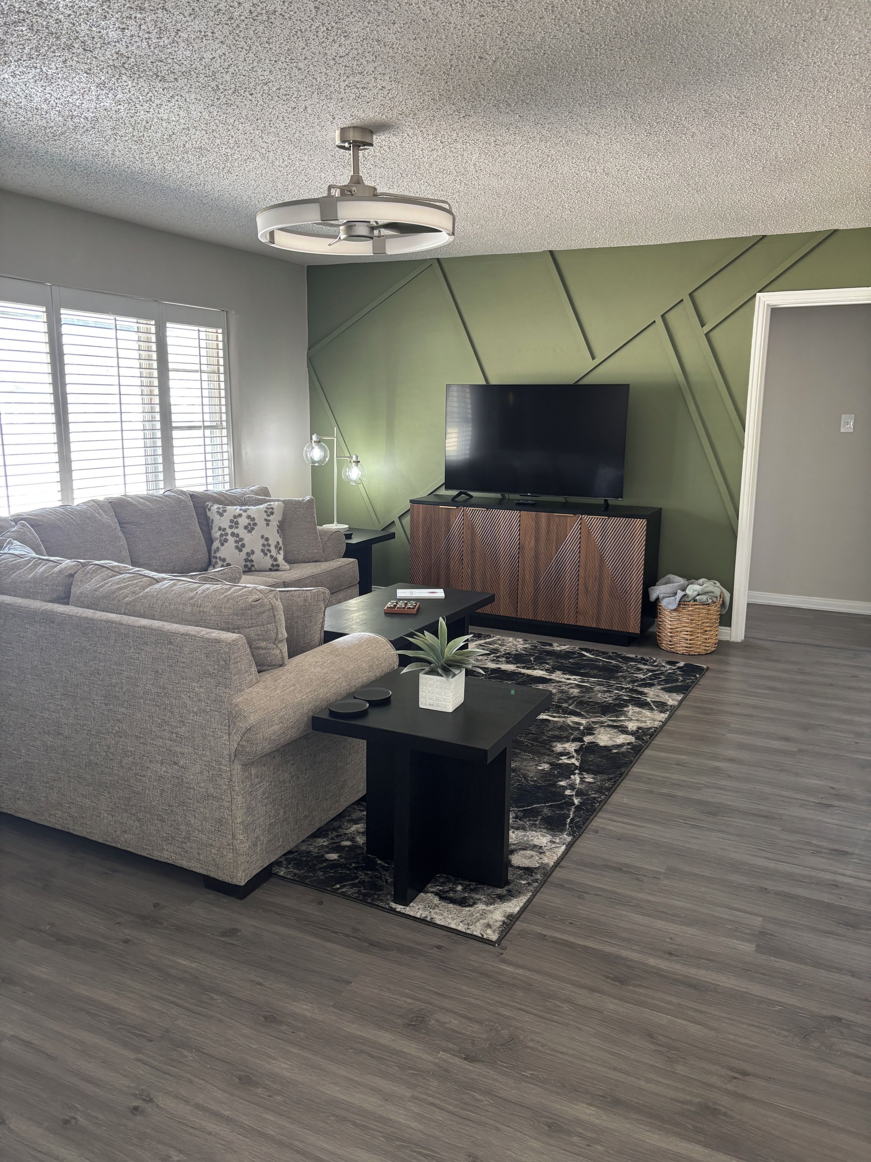 A modern living room with a sectional sofa, a flat-screen TV, a coffee table, and a patterned rug.