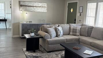 Een woonkamer met een hoekbank, een salontafel, een vloerkleed en een hanglamp.