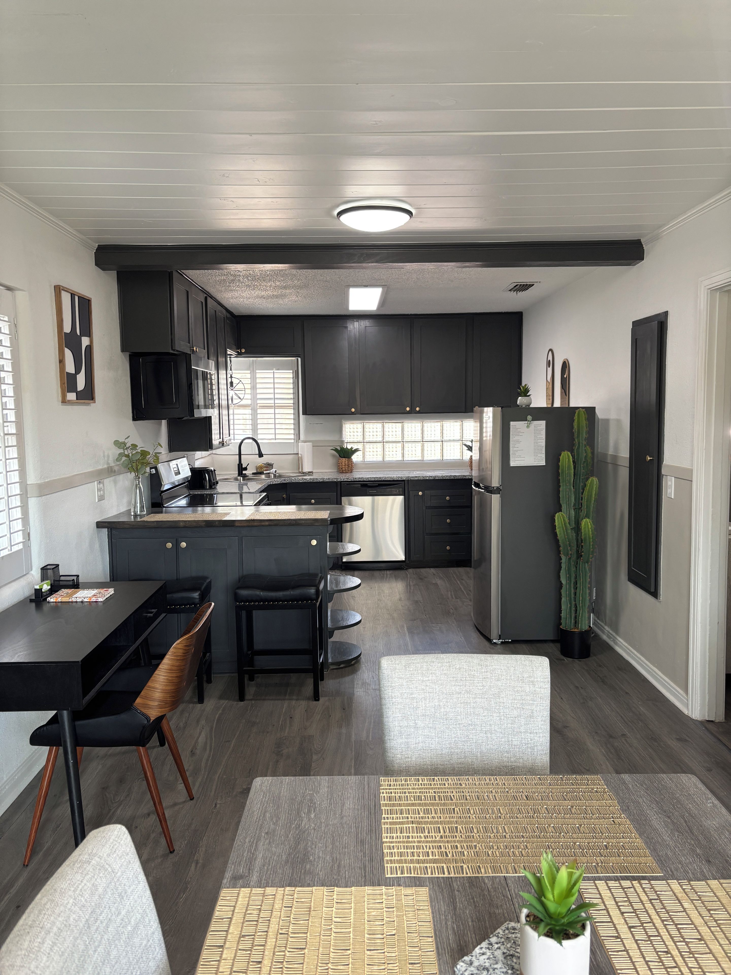 A modern kitchen with dark cabinetry, stainless steel appliances, a central island, and a dining area with a bench and chairs.