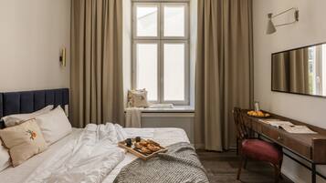 Habitación de hotel con cama, escritorio, silla, ventana con cortinas y bandeja con pasteles.