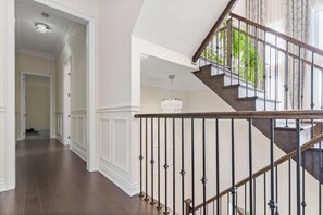 Un interior moderno con una escalera de madera, paredes blancas y un pasillo que conduce a otra habitación.