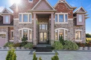 A two-story house with a stone facade, multiple windows, and a front porch. - Estate Villa, 6,600 Sqft, 1-acre, 6 Bed, 7 Bath (Whitchurch-Stouffville)