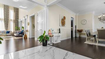 A spacious living room with a marble floor, a dining area with a chandelier, and a kitchen with white cabinetry.
