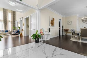 Una sala de estar amplia con piso de mármol, un comedor con candelabro y una cocina con muebles blancos.