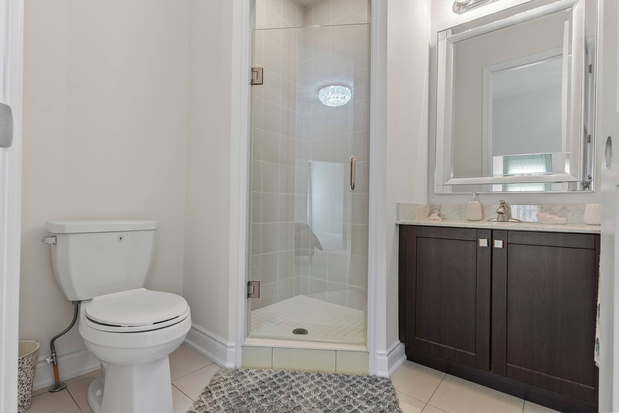 A bathroom with a toilet, a glass-enclosed shower, and a dark wooden vanity with a mirror.