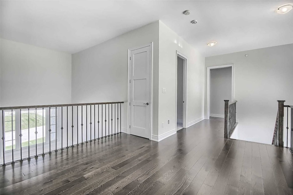A spacious interior with a wooden floor, white walls, and a balcony with a metal railing.