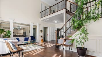 Amplia sala de estar con techo alto, una escalera y una gran planta en maceta.