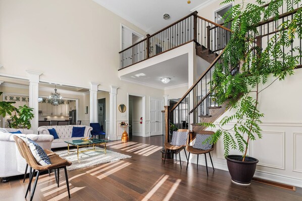 A spacious living area with a high ceiling, a staircase, and a large potted plant.