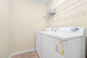 A laundry room with two stacked front-loading washing machines, a metal drying rack, and a tiled floor. - Family Villa Near Disney, Pool & 2 Suites (Kissimmee)