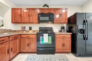 A kitchen with wooden cabinets, a black microwave, a stainless steel refrigerator, a black oven, and a coffee maker. - Family Villa Near Disney, Pool & 2 Suites (Kissimmee)