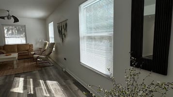 A living room with a sofa, chairs, a coffee table, a floor lamp, and a large window with blinds.