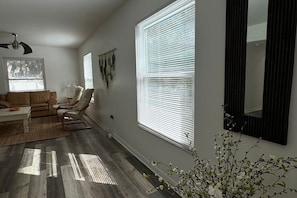 Un salon comprenant un canapé, des fauteuils, une table basse, un lampadaire et une grande fenêtre avec des stores.