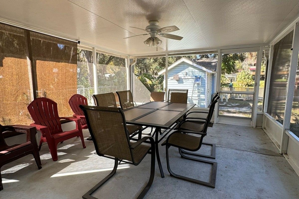 Une terrasse couverte avec une table et des chaises, de grandes fenêtres et un ventilateur de plafond.