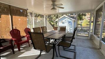 A covered patio with a table and chairs, large windows, and a ceiling fan.